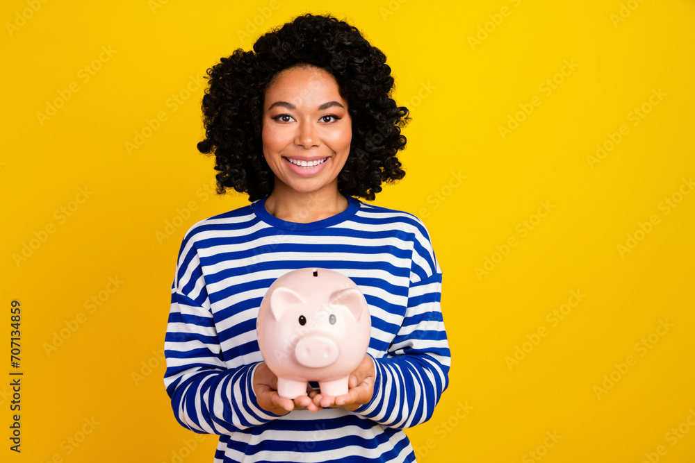Photo of good mood toothy beaming woman with chevelure dressed striped sweatshirt hold piggy box isolated on yellow color background Photo of good mood toothy beaming woman with chevelure dressed striped sweatshirt hold piggy box isolated on yellow color background