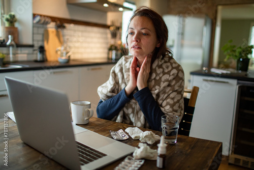 Woman feeling sick with sore throat and flu symptoms working on laptop at home photo