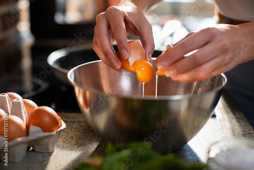 Woman cracking an egg into a bowl for cooking at home kitchen photo