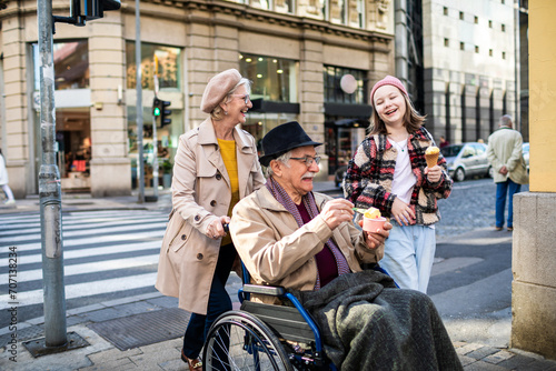Happy grandparents with granddaughter eating ice cream on city street photo