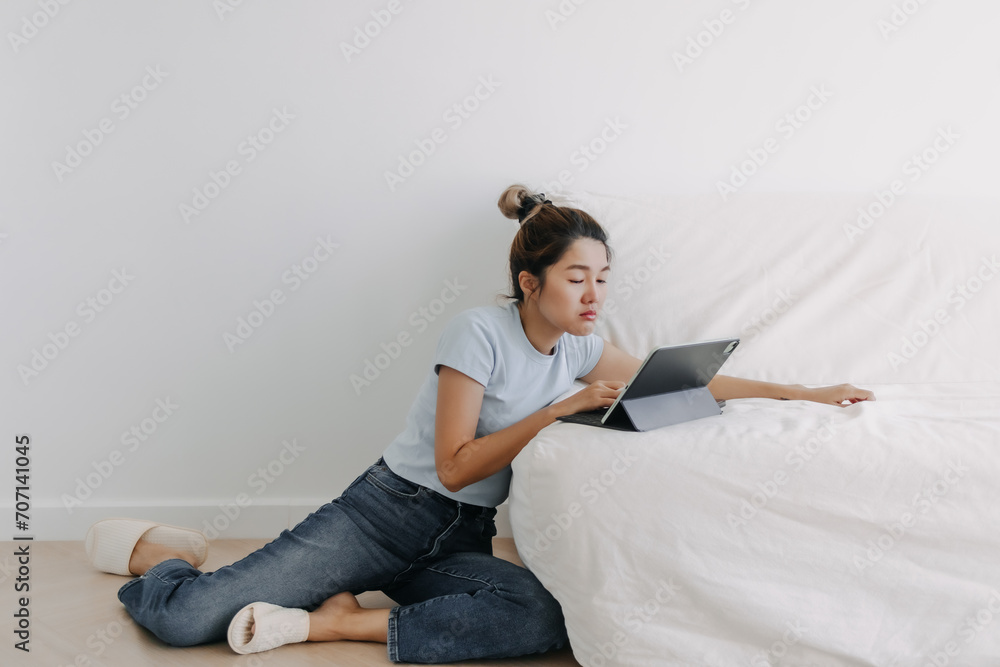 Asian young Thai woman sitting on floor and leaning on white sofa while using tablet in apartment room, tired sleepy and drowsiness while working on computer alone. Asian young Thai woman sitting on floor and leaning on white sofa while using tablet in apartment room, tired sleepy and drowsiness while working on computer alone.