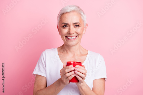 Photo portrait of pretty retired female hold red coffee cup teatime dressed stylish white outfit isolated on pink color background