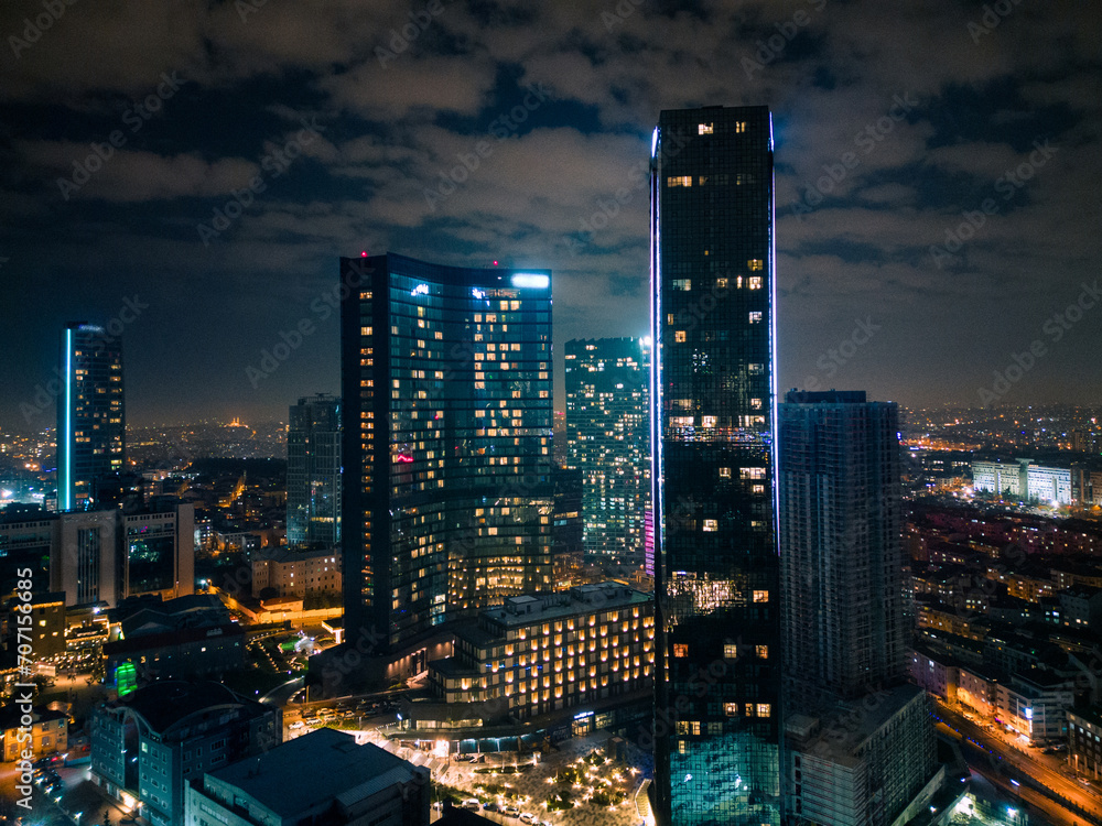 Naklejka premium Istanbul's glass and concrete skyscrapers, home to offices, hotels, and residential complexes at night. Aerial drone view