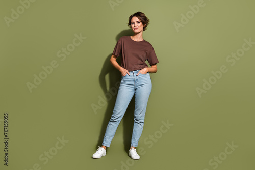 Full length photo of adorable nice girl wear oversize t-shirt standing arms in denim pants pockets isolated on green color background © deagreez