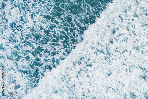 Aerial top view of white foam on the surface of the blue sea.