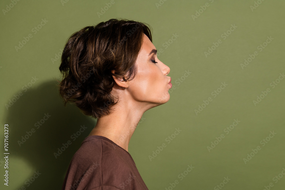Side profile portrait of pretty woman with short hairdo wear t-shirt send air kiss to empty space isolated on green color background Side profile portrait of pretty woman with short hairdo wear t-shirt send air kiss to empty space isolated on green color background