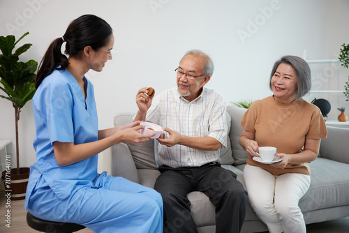 nurse or caregiver giving chocolate cookies to senior couple at home