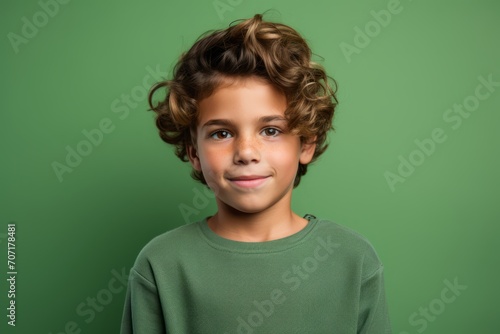 Portrait of a cute little boy with curly hair over green background