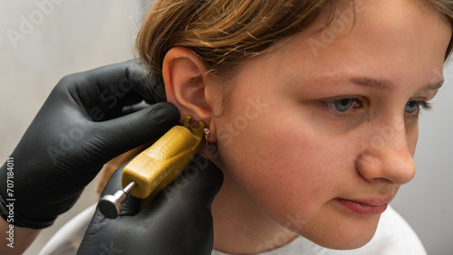 A doctor wearing sterile black medical gloves pierces the ears of a young pretty girl. Girls get their ears pierced. The process of piercing a child's ears in a beauty salon with a piercing gun photo