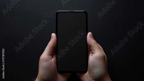 Front view of hands gripping a mobile with a blank screen mockup, the camera focusing on the device's potential for creative customization against a sleek black background photo