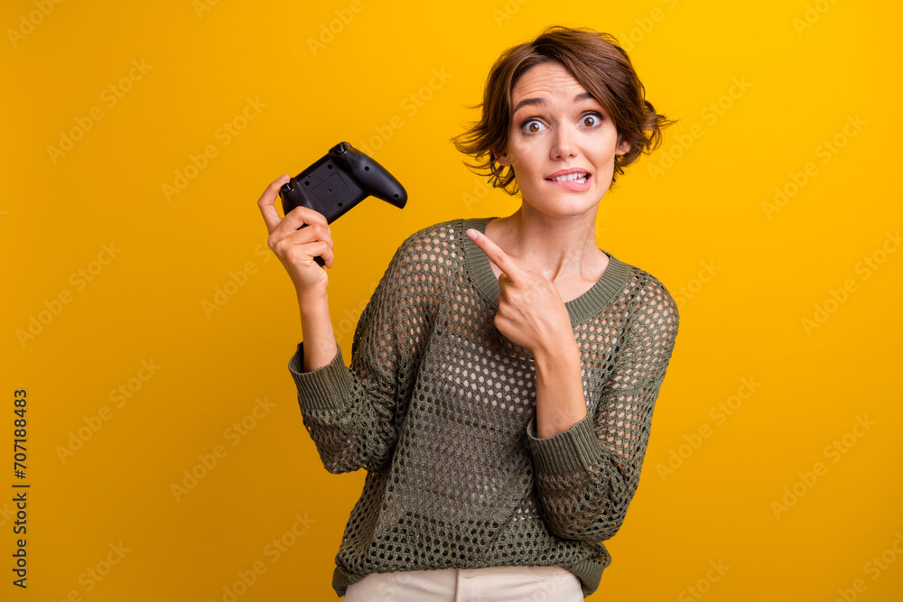 Naklejka premium Photo of lovely young lady point amazed joystick play station dressed stylish knitted khaki garment isolated on yellow color background
