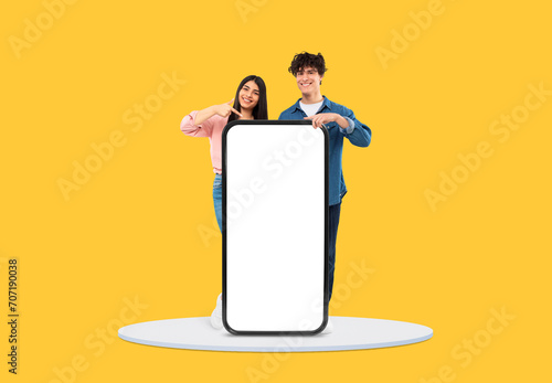 Cheerful young duo pointing at blank mobile screen