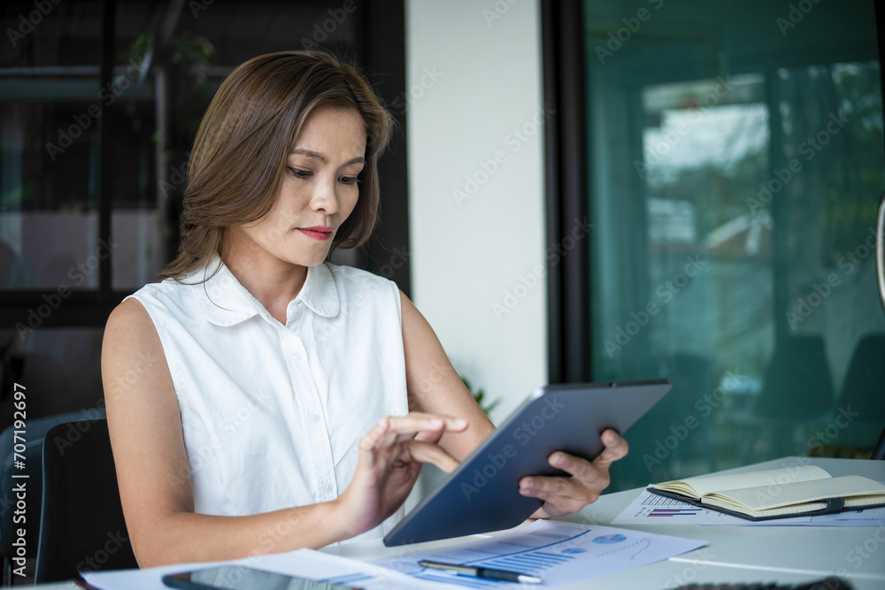 Businesswoman sitting at desk on couch in workplace or at home working on laptop and analyzing data on charts and graphs and writing on papers to make business plan and strategies for company, 