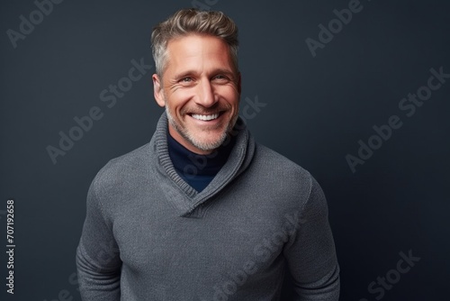 Handsome middle-aged man in sweater and scarf smiling at camera.