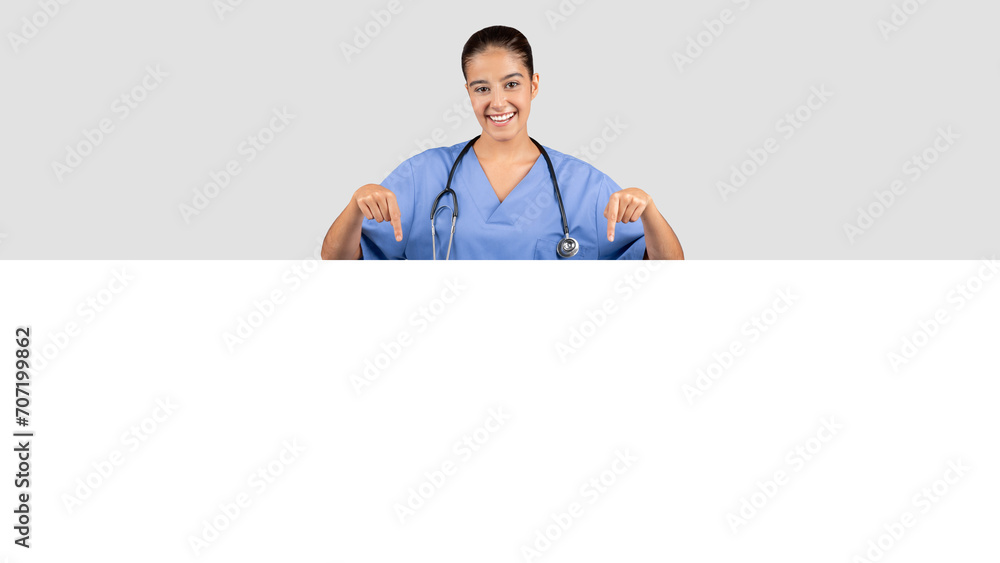 Radiant European millennial medical worker in a blue uniform pointing downwards Radiant European millennial medical worker in a blue uniform pointing downwards