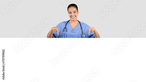 Radiant European millennial medical worker in a blue uniform pointing downwards
