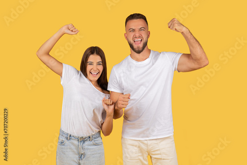 Excited young couple in white t-shirts showing off their muscles and celebrating success