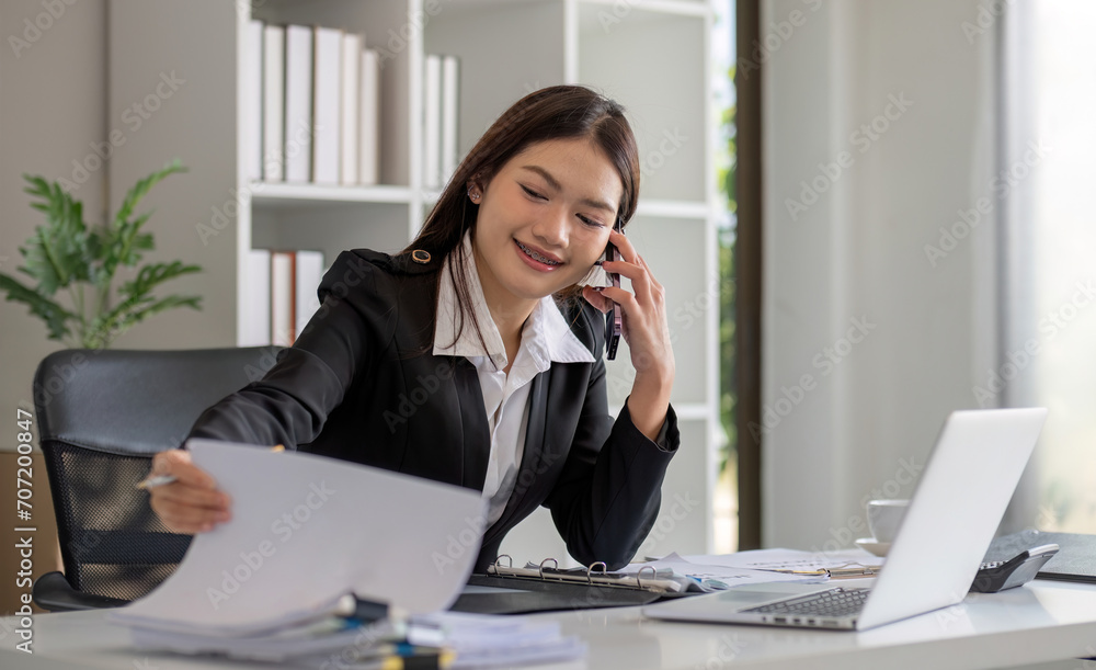 Cheerful Asian businesswoman talking on the phone working in modern office Happy Asian businesswoman company manager wearing a suit is talking on the phone sitting in the office. Cheerful Asian businesswoman talking on the phone working in modern office Happy Asian businesswoman company manager wearing a suit is talking on the phone sitting in the office.
