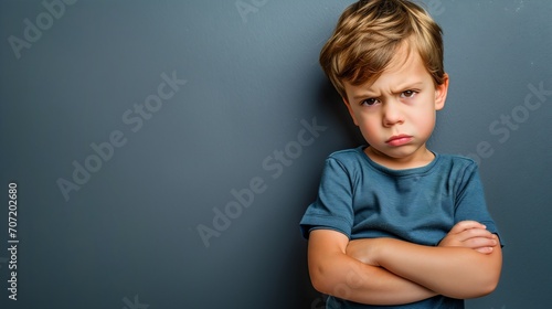 Mad male kid, angry little boy standing with his arms crossed, and looking at the camera with upset face expression. Unhappy toddler, studio shot, annoyed and frustrated child emotion photo