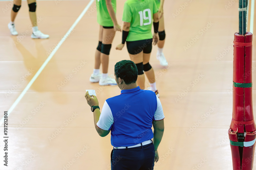 Back view of male second volleyball referee stands and assists the main referee in the game on the volleyball court. Volleyball referee shows various gestures in deciding the volleyball women game.