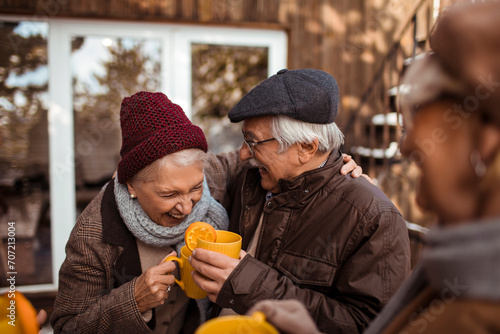 Happy senior couple drinking warm drinks with friends outside in winter photo