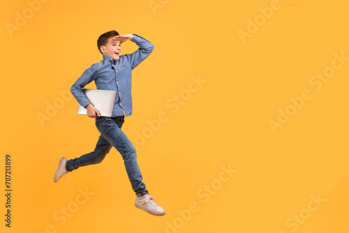 Teen boy holding laptop while running on yellow background