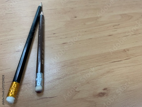 Two pencils on the wooden table surface, black pencil