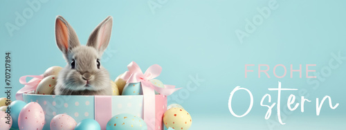 Frohe Ostern Konzept Feiertag Grußkarte mit deutschem Text - Cooler Osterhase, Kaninchen, sitzt in Geschenkbox mit Ostereiern, isoliert auf blauem Hintergrund.