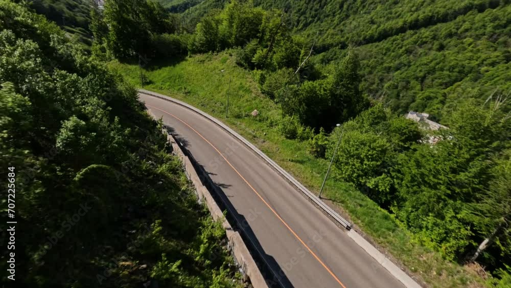 Aerial panorama view flight over empty asphalt serpentine road sunny alpine resort landscape FPV sports drone shot. Speed white car fast riding on mountain slope highway surrounded by greenery and sky Aerial panorama view flight over empty asphalt serpentine road sunny alpine resort landscape FPV sports drone shot. Speed white car fast riding on mountain slope highway surrounded by greenery and sky
