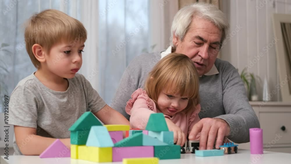 Grandfather playing toys with grandson and young granddaughter indoor. Old man grandpa studying with his grandchildren at weekend. Senior male having fun with kids. Happy multigeneration family video Grandfather playing toys with grandson and young granddaughter indoor. Old man grandpa studying with his grandchildren at weekend. Senior male having fun with kids. Happy multigeneration family video