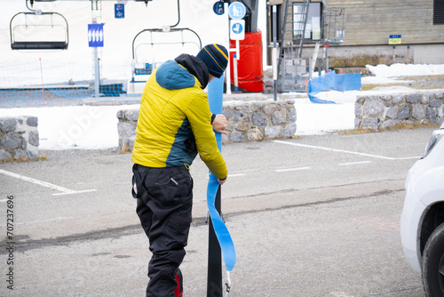 Принти на полотні man putting sealskin on skis in parking lot, next to camper van, ski lift in the background