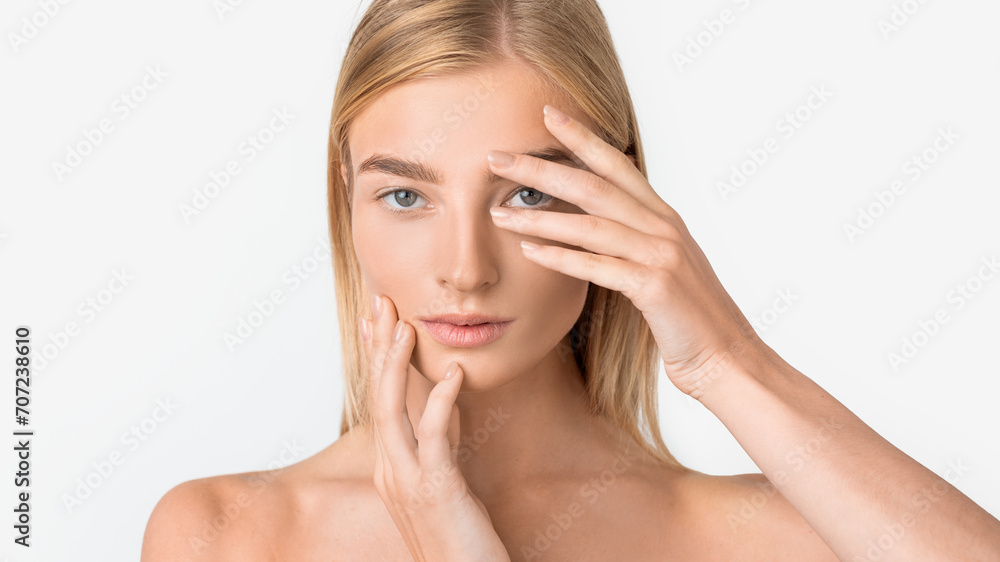 attractive blonde woman looks at camera while touching face, studio