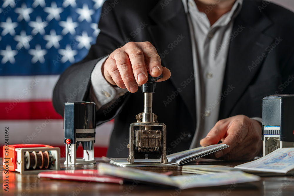 Immigration and passport control on the American flag background, closeup. Vacation and travel concept. Immigration border control officer will arrival stamp in the international passport at airport