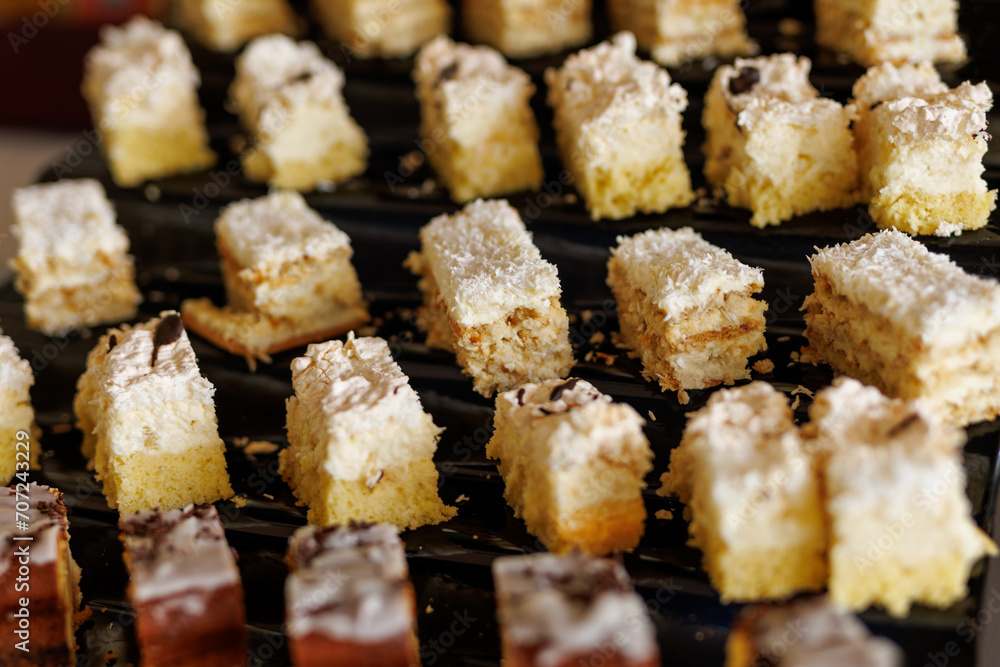 Bite-sized coconut cakes with white frosting on a black tray Bite-sized coconut cakes with white frosting on a black tray