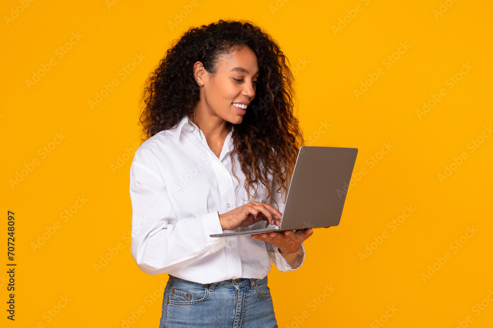 Happy african american lady using her laptop computer, yellow background Happy african american lady using her laptop computer, yellow background