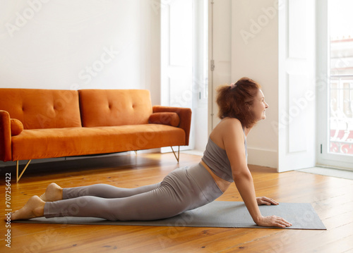 Senior lady training at home, making Cobra pose on yoga mat,