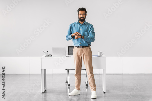 Indian businessman checking time, standing by office desk