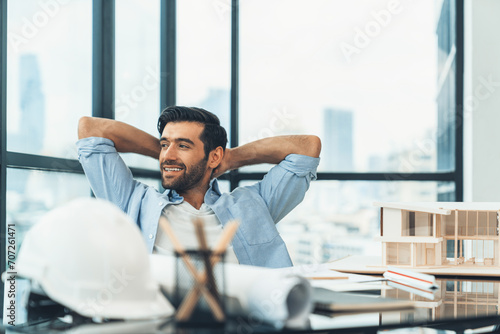 Portrait of relaxed young architect engineer resting and designing while sitting in modern home office. Male worker or manager take a break, holding hands behind head after finish project. Tracery photo