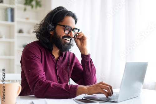 Smiling Young Indian Man Wearing Headset Working On Laptop Computer