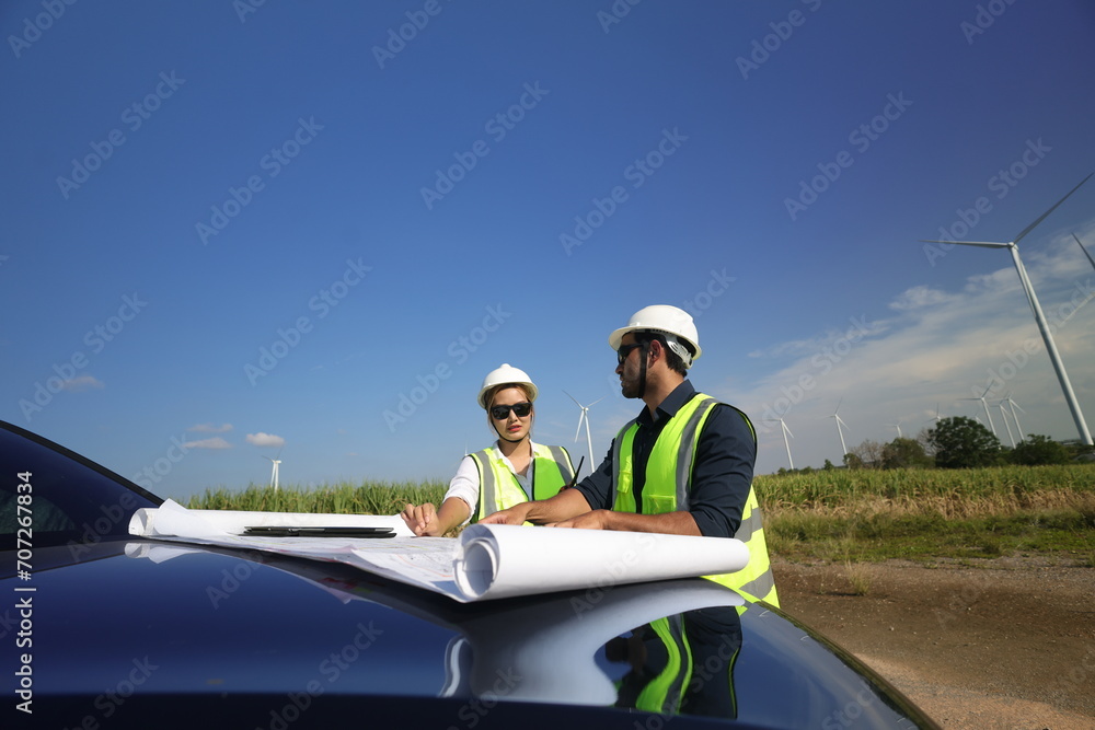 Wind turbine engineers working on the roof of car at a wind turbine field, checking and comparing the blueprint and condition of the Turbine's Electrical Power