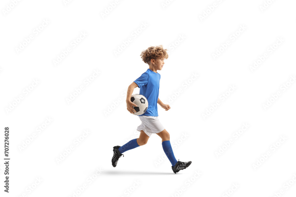 Full length profile shot of a boy in a football kit running with a ball