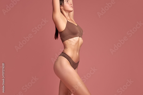 Depilation  epilation  laser hair removal. Cropped female body  woman in underwear with raised hands standing against pink background. Smooth skin. Concept of natural beauty  health and body care