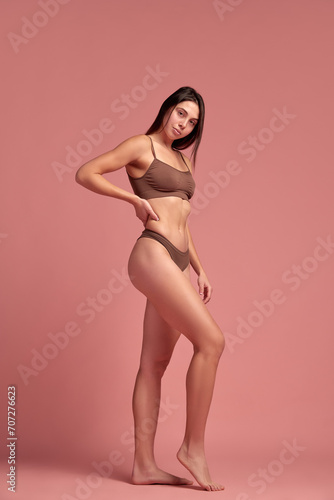 Loosing weight in healthy way. Young beautiful woman with slim body standing in cotton underwear against pink studio background. Concept of natural beauty, health and body care, diet, nutrition