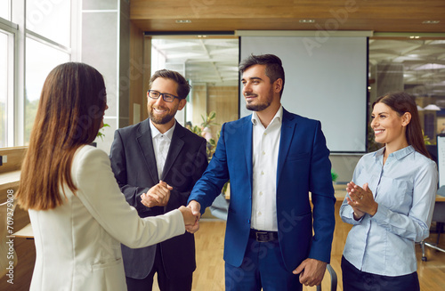 Group of business people in suits meeting in the office, making a deal and exchanging handshakes. Happy man and woman shake hands while colleagues applaud. Professional cooperation, teamwork concept photo