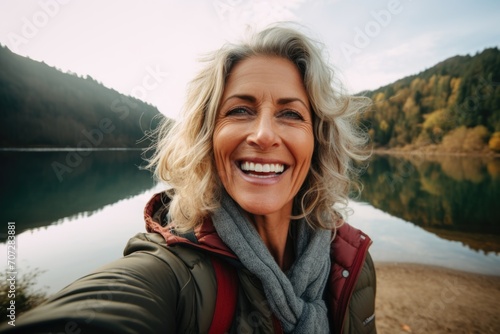 Smiling middle aged woman taking selfie lakeside