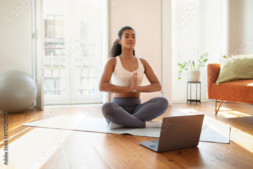 Sporty young woman engaging in online yoga class at home