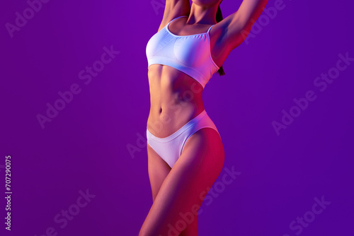 Depilation, epilation, laser hair removal. Cropped female body, woman in underwear with raised hands standing against purple background in neon light. Smooth skin. Concept of beauty, health, body care