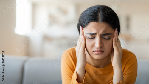 Stressed young indian woman suffering from severe headache or migraine at home photo