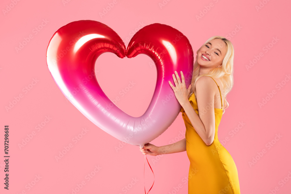 Blissful blonde woman hugging heart balloon on pink background Blissful blonde woman hugging heart balloon on pink background