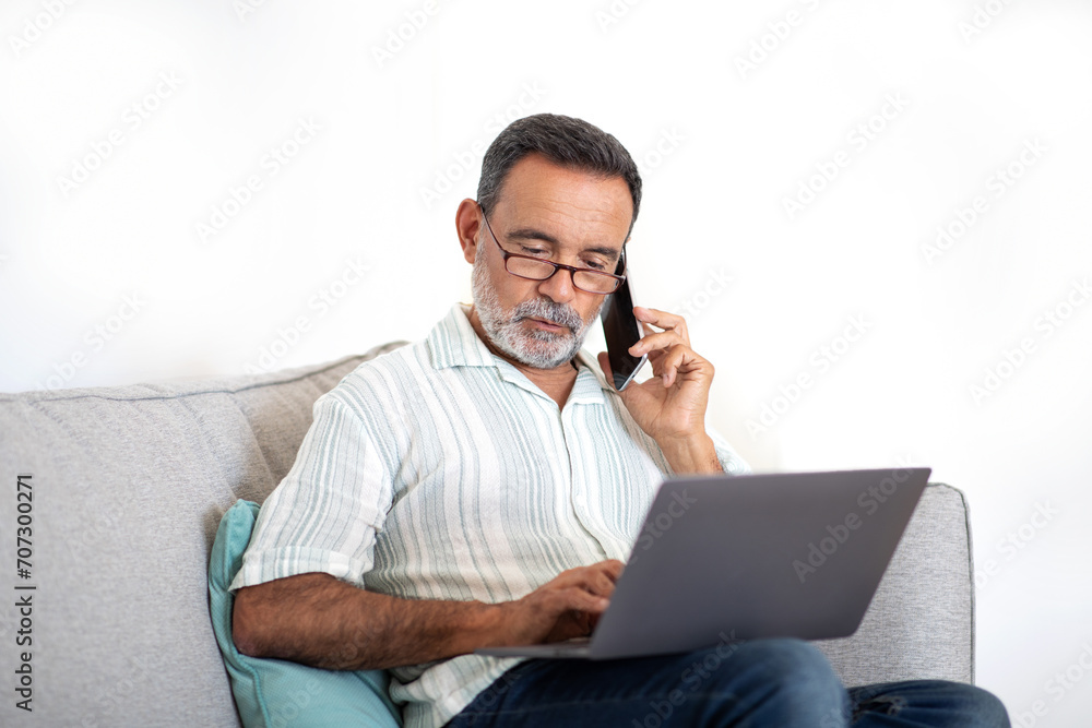 Senior Man Talks on Cell Phone Working On Laptop Indoors Senior Man Talks on Cell Phone Working On Laptop Indoors